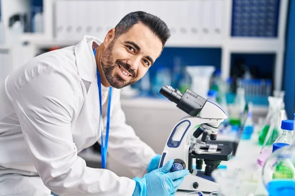 Laboratuvarda mikroskop kullanarak gülümseyen genç İspanyol bilim adamı.