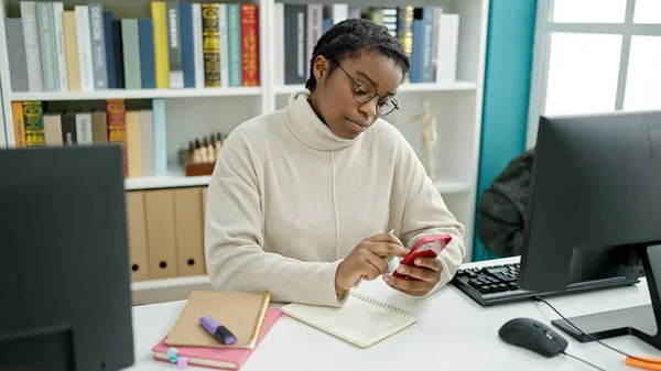 図書館大学でコンピュータとスマートフォンを使うアフリカ系アメリカ人女性学生 — ストック写真