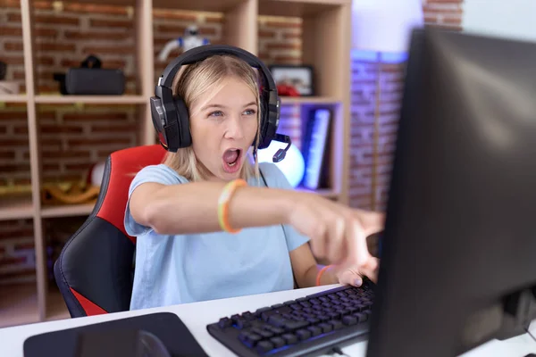 Mladá Běloška Hraje Videohry Sluchátkách Ukazujíc Prstem Překvapeně Dopředu Otevřenými — Stock fotografie