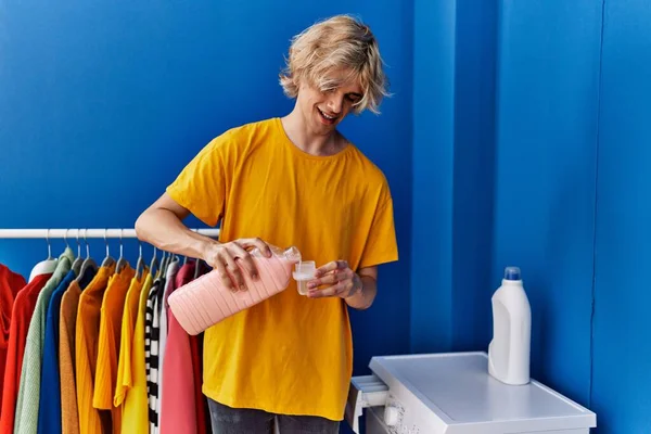 年轻的金发男子微笑着 自信地把洗涤剂倒进洗衣房 — 图库照片