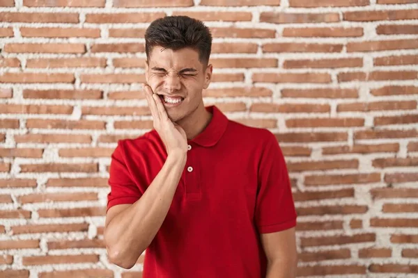 年轻的惊慌失措的男人站在砖墙上 用手触摸着嘴 因为牙齿疼痛或牙病而带着痛苦的表情 — 图库照片