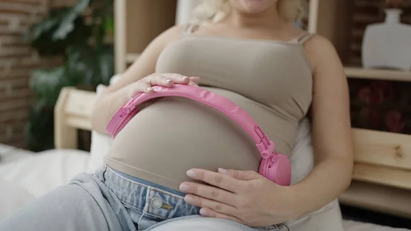 若いです妊娠中の女性置くヘッドフォンオン腹にベッドルーム — ストック写真