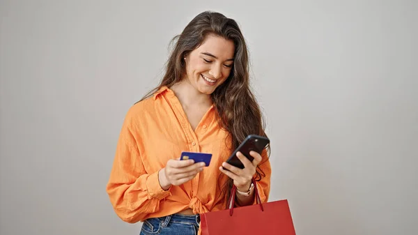 若い美しいヒスパニック系の女性が隔離された白い背景の上にスマートフォンやクレジットカードを使用してショッピングバッグを保持 — ストック写真
