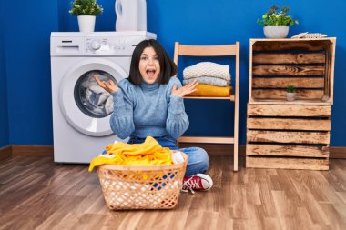 Çamaşırhanede zaferi kutlayan genç İspanyol kadın mutlu bir gülümseme ve kaldırılmış ellerle kazanan bir ifadeyle. 