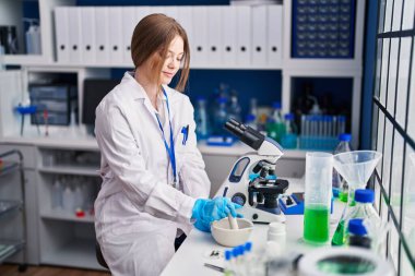 Genç beyaz kadın bilim adamı laboratuarda çalışırken gülümsüyor.