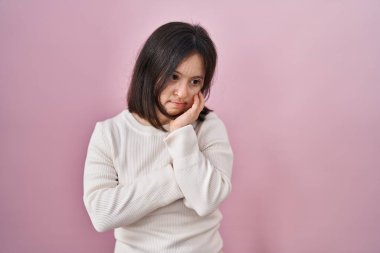 Pembe arka planda duran Down sendromlu kadın çapraz kollu depresyon sorunlarından yorgun ve sıkılmış göründüğünü düşünüyor.. 