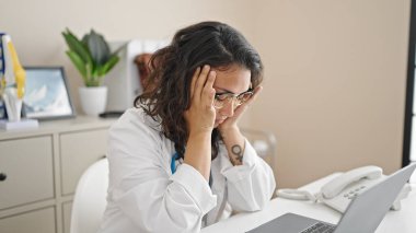 Young beautiful hispanic woman doctor stressed working at clinic