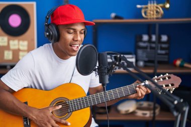 Genç Latin müzisyen müzik stüdyosunda klasik gitar çalarak şarkı söylüyor.