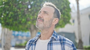 Orta yaşlı bir adam parkta ciddi bir ifadeyle gökyüzüne bakıyor.