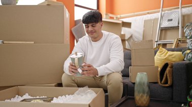 Young hispanic man unpacking cardboard box at new home