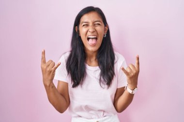 Genç İspanyol kadın pembe arka planda duruyor çılgın bir ifadeyle bağırıyor elleri havada rock sembolü yapıyor. Müzik yıldızı. ağır müzik konsepti. 