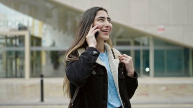 Young beautiful hispanic woman student smiling confident talking on smartphone at street