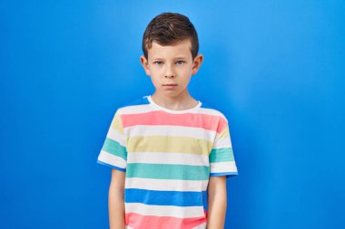 Mavi arka planda duran genç beyaz çocuk şüpheci ve gergin, sorun yüzünden surat asıyor. negatif kişi. 