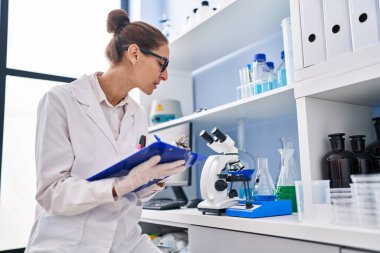 Young woman scientist measuring liquid writing on clipboard at laboratory