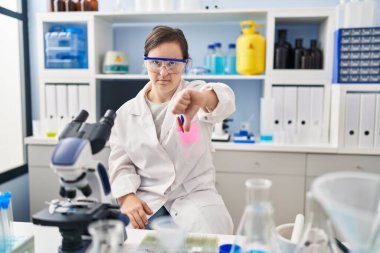 Down sendromlu İspanyol kız, bilim adamı laboratuarında çalışıyor. Mutsuz ve sinirli görünüyor. Reddedilmiş görünüyor. kötü ifade. 