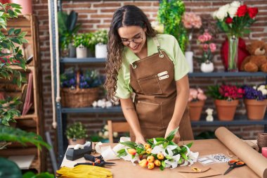 Young beautiful hispanic woman florist make bouquet of flowers at flower shop