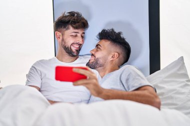 Genç çift akıllı telefondan video izliyor. Yatak odasında yatıyorlar.