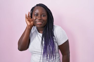 Pembe arka planda dikilen genç Afrikalı bir kadın kulağından kulaklarına gülümseyerek dedikodulara ve dedikodulara kulak veriyor. Sağırlık kavramı. 