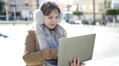Young blonde woman using laptop sitting on bench at street