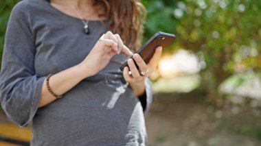 Parkta akıllı telefon kullanan hamile bir kadın.