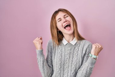 Pembe arka planda duran güzel kadın şaşırmış ve şaşırmış bir şekilde kollarını kaldırmış ve gözlerini kapatmış bir şekilde başarıyı kutluyor. Kazanan konsept. 