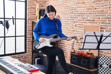 Müzik stüdyosunda gitar çalarken kendinden emin gülümseyen Çinli kadın sanatçı.