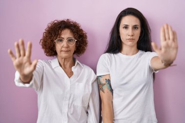 İspanyol anne ve kızı pembe arka plan üzerine gündelik beyaz tişört giyip avuç içiyle şarkı söylemeyi bırakıyorlar. Yüzünde olumsuz ve ciddi bir jest olan uyarı ifadesi. 