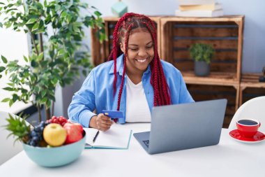 Laptop kullanan ve evde kredi kartı tutan Afrikalı Amerikalı bir kadın.