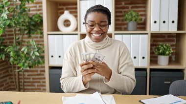 Afrikalı Amerikalı kadın iş adamı ofiste dolar sayıyor.