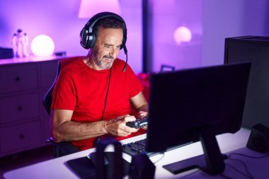 Middle age man streamer playing video game using joystick at gaming room