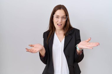 Güzel esmer kadın iş ceketi ve gözlük takıyor. Neşeli gülümsüyor ve kollarını açıyor. Hoş geldin, olumlu ve kendinden emin selamlar. 