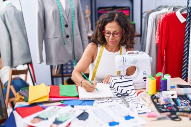 Orta yaşlı kadın elbise fabrikasında defter çiziyor.