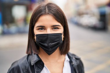 Genç, güzel, İspanyol bir kadın sokakta maske takarak gülümsüyor.
