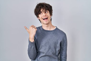 İzole edilmiş arka planda duran genç adam gülümsüyor, gülümsüyor ve başparmağıyla yan tarafa bakıyor.. 