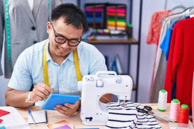 Genç Çinli terzi terzide dokunmatik ped kullanarak gülümsüyor.