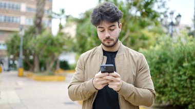 Genç İspanyol bir adam parkta akıllı telefon kullanıyor.