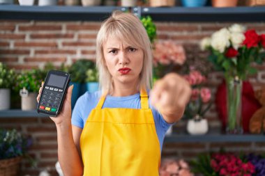 Çiçekçide çalışan beyaz bir kadın elinde veri bankasıyla kamerayı ve seni işaret ediyor. Kendine güveni tam bir jest. 