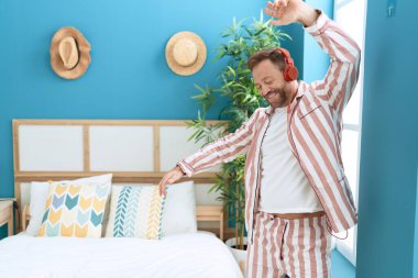 Orta yaşlı bir adam gülümseyerek yatak odasında dans ediyor.