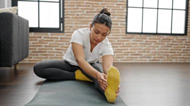 Genç, güzel, İspanyol bir kadın evde yerde oturmuş bacaklarını açıyor.