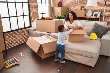 Mother and son unpacking cardboard box sitting on sofa at new home