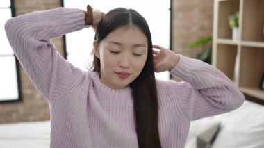 Young chinese woman waking up stretching arms at bedroom