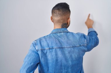 Genç İspanyol adam izole edilmiş arka planda dikiliyor. Parmak eliyle geriye doğru poz veriyor. 