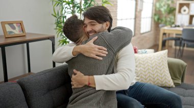 İki erkek kanepede oturup birbirlerine sarılıyorlar.