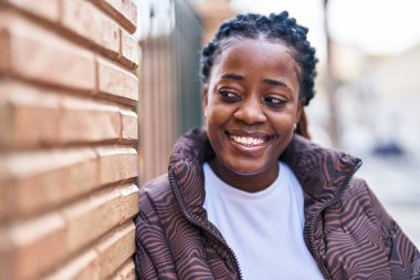 Afro-Amerikalı kadın gülümsüyor. Kendinden emin bir şekilde caddeye bakıyor.