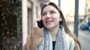 Genç sarışın kadın gülümsüyor. Kendine güveni tam. Akıllı telefondan konuşuyor.