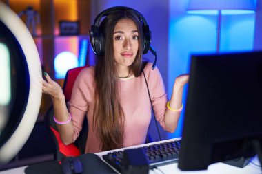 Genç İspanyol kadın video oyunları oynuyor, elleri ve kolları havada ve kafası karışmış bir ifade. şüphe kavramı. 