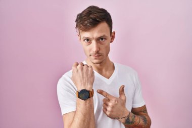 Pembe arka planda dikilen beyaz adam acele ederek zamanı, sabırsızlığı ve rahat bir ifadeyle kameraya bakıyor. 