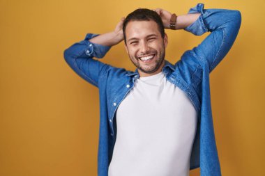 Sarı arka planda dikilen İspanyol adam komik ve çılgın poz veriyor parmakları kafasında tavşan kulakları, neşeli bir gülümseme 