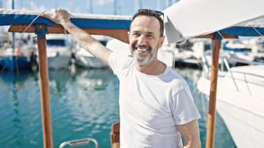 Orta yaşlı bir adam teknede güneş gözlüğü takarak gülümsüyor.