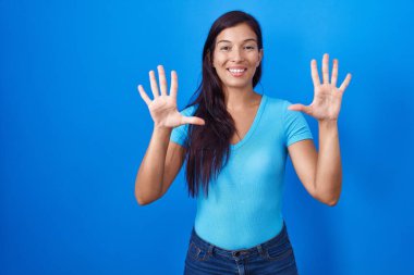 Mavi arka planda duran genç İspanyol kadın on numarayı gösterip işaret ederken kendinden emin ve mutlu bir şekilde gülümsüyor.. 